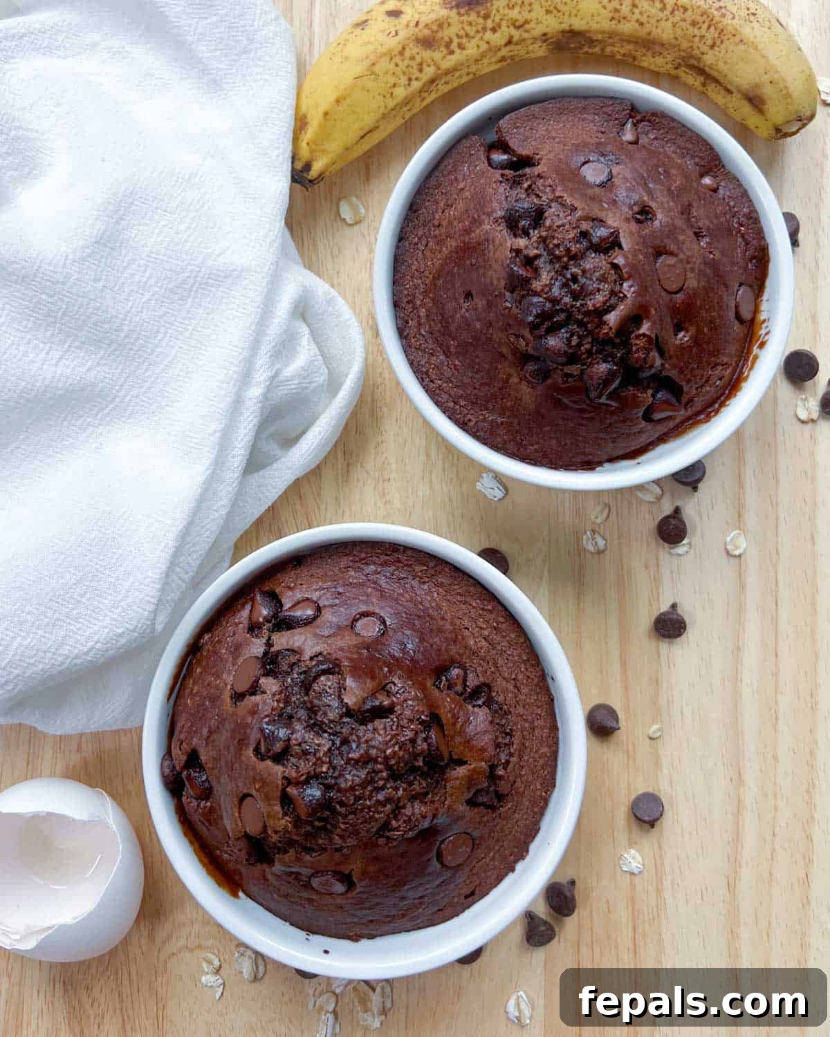 Decadent Chocolate Protein Baked Oats 8 Two baked oats ramekins are displayed side-by-side, with extra chocolate chips scattered around them.