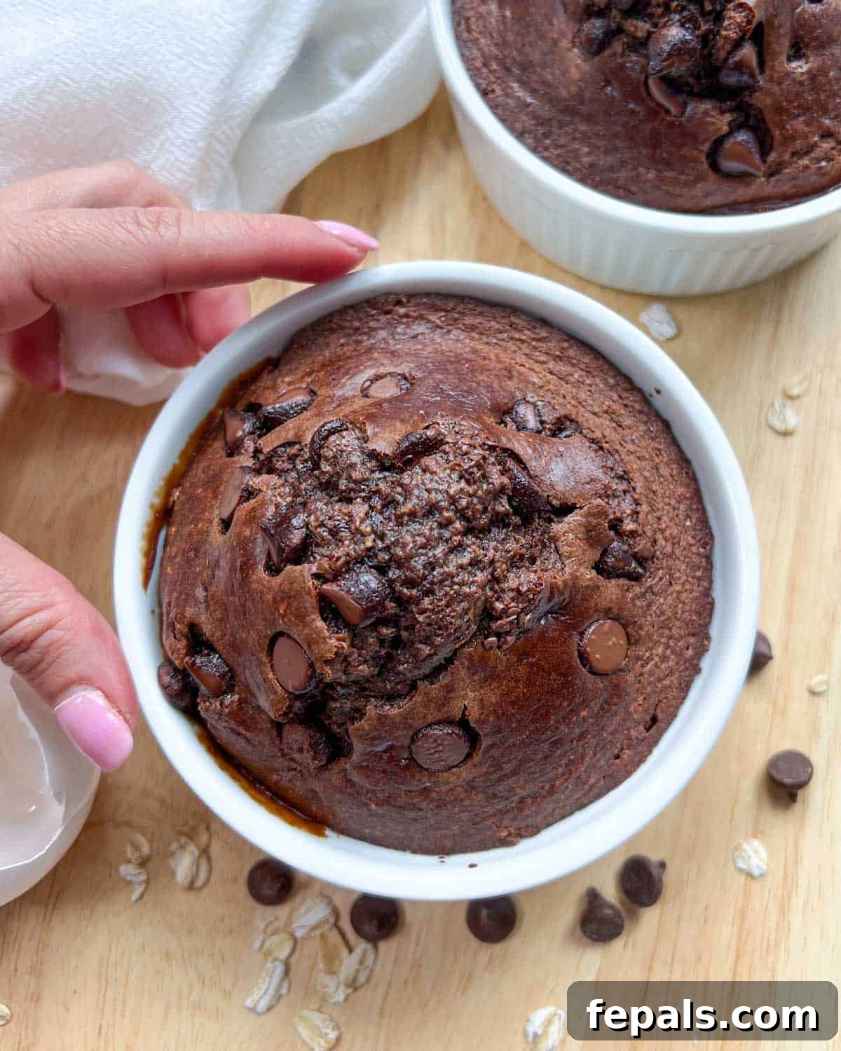 Decadent Chocolate Protein Baked Oats 9 One hand holds a ramekin filled with freshly baked chocolate protein oats, ready to be enjoyed.