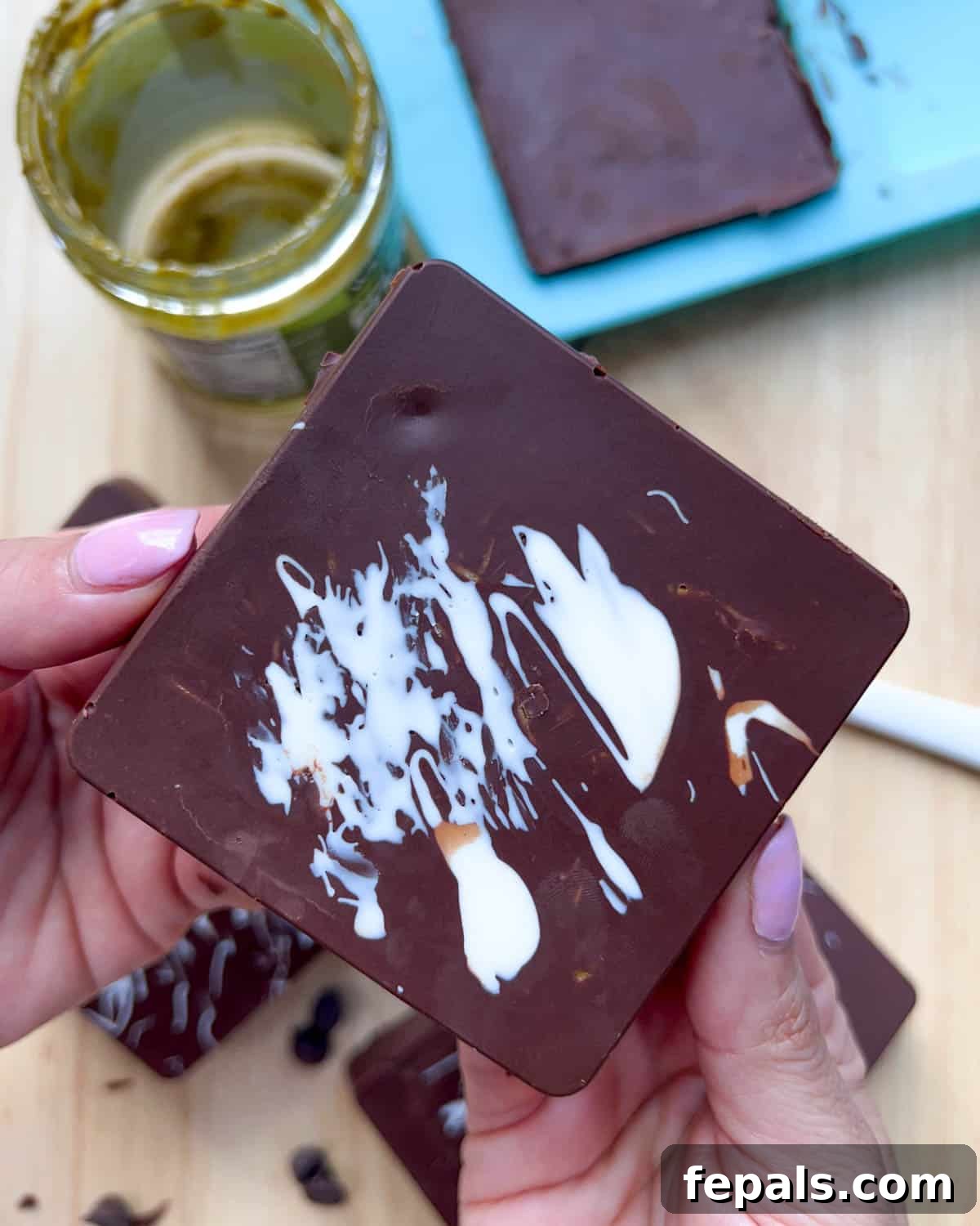 Hand holding a square chocolate bar, showing the rich dark chocolate exterior.