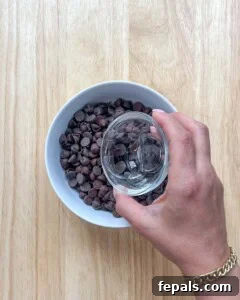 Adding coconut oil to dark chocolate chips in a bowl for melting.