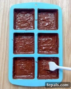 Spreading melted chocolate evenly along the bottom and sides of a silicone mold.