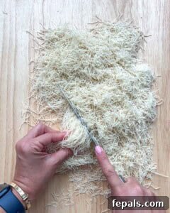Chopping kataifi pastry dough on a wooden cutting board.