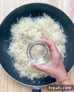 Adding coconut oil to chopped kataifi in a pan over medium heat.