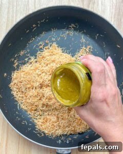 Pouring creamy pistachio butter over toasted kataifi in a pan.