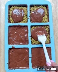 Adding the final layer of melted chocolate over the pistachio filling in the molds.