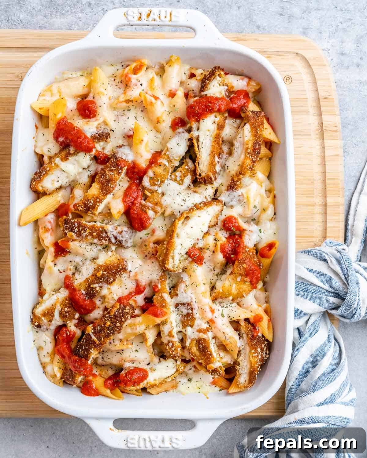 Ultimate Chicken Parm Bake 2 A baking white dish with pasta and tomato sauce topped with crispy chopped chicken and melted cheese, ready to serve.