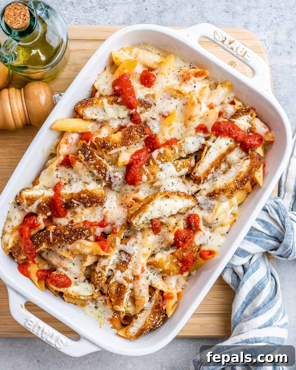 Ultimate Chicken Parm Bake 9 White casserole dish with a chicken and pasta casserole, topped with fresh herbs.