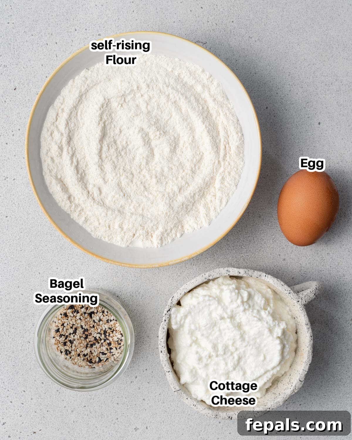 Protein Packed Cottage Cheese Bagels Yeast Free 3 A selection of ingredients laid out on a surface, including cottage cheese, flour, an egg, and a jar of everything bagel seasoning.