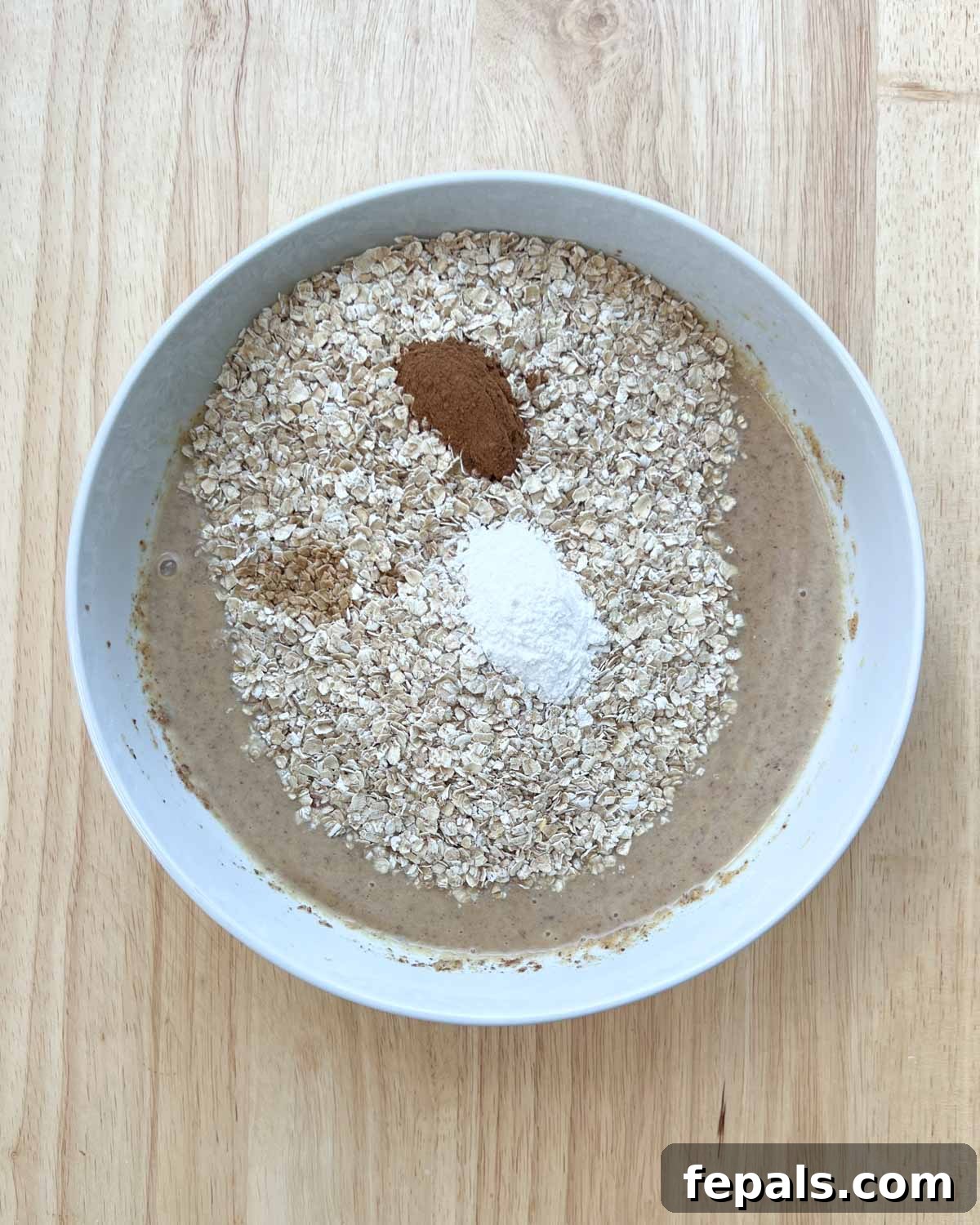 Cozy Apple Oat Squares 6 Oats, baking powder, and cinnamon added to the wet peanut butter mixture in a mixing bowl.