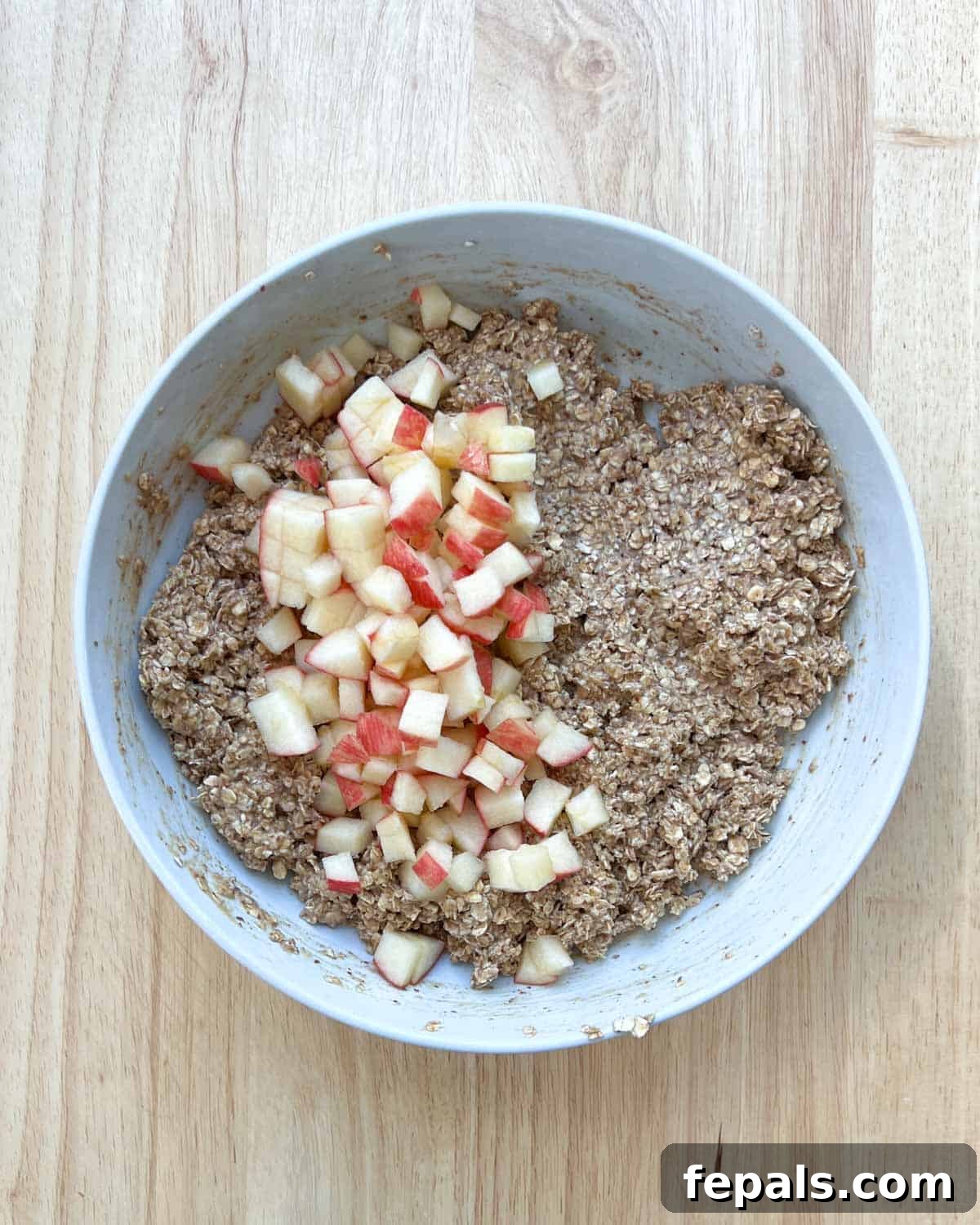 Cozy Apple Oat Squares 7 Finely chopped apples being gently folded into the oat mixture in a round bowl.