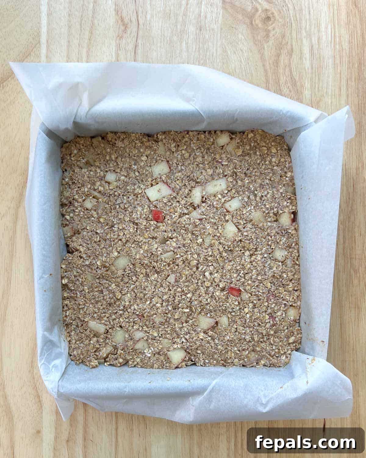 Cozy Apple Oat Squares 8 The apple oatmeal batter spread evenly into a square baking pan lined with parchment paper, ready for the oven.