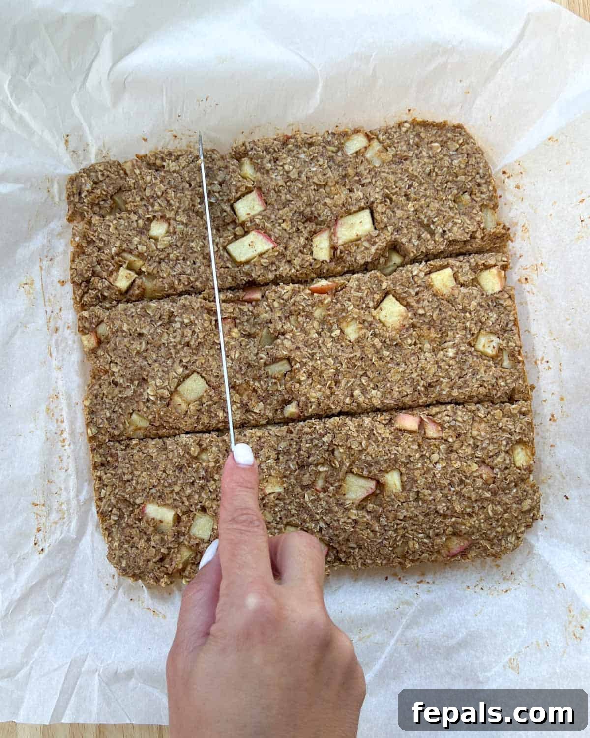 Cozy Apple Oat Squares 9 A hand using a knife to cut the cooled apple oatmeal bars into squares within the baking pan.