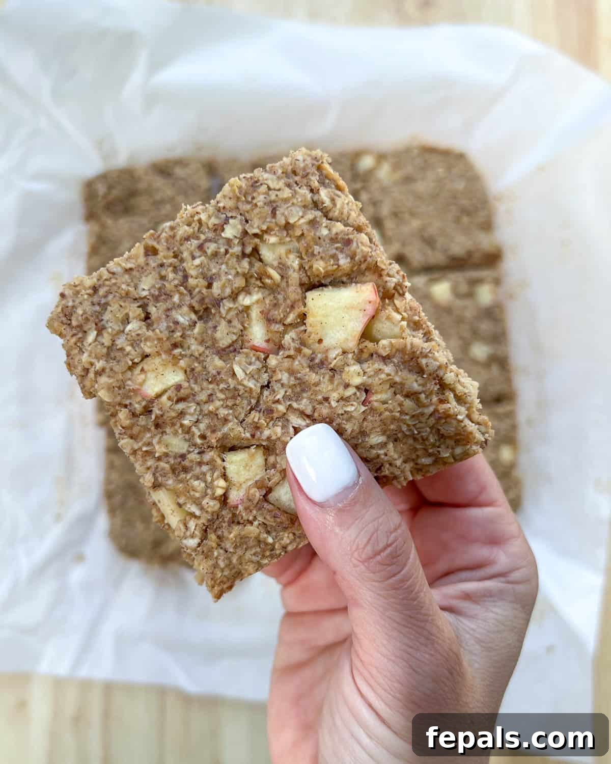 Cozy Apple Oat Squares 10 A hand delicately holding a single apple oatmeal bar, showcasing its moist texture and apple chunks.