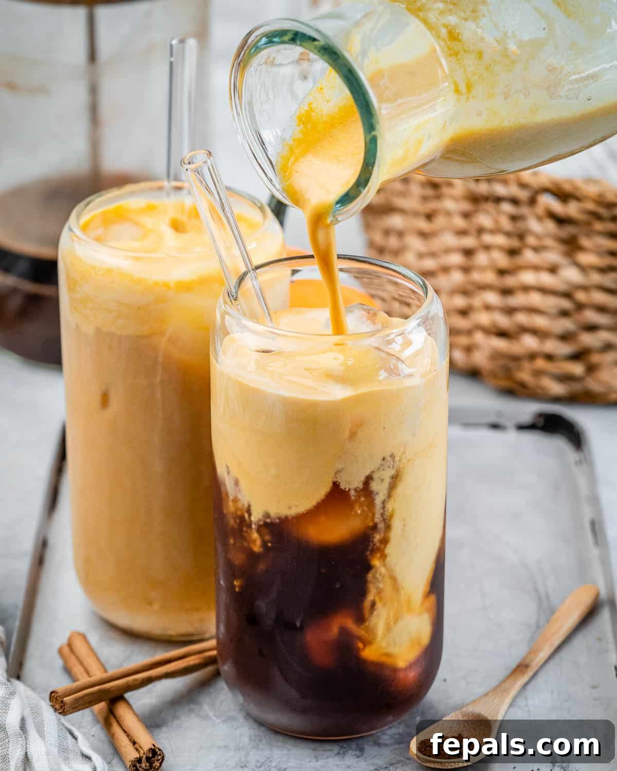 Step 5: Artfully pouring the freshly blended pumpkin cream over cold brew coffee and ice in a tall glass, creating a beautiful layered effect.