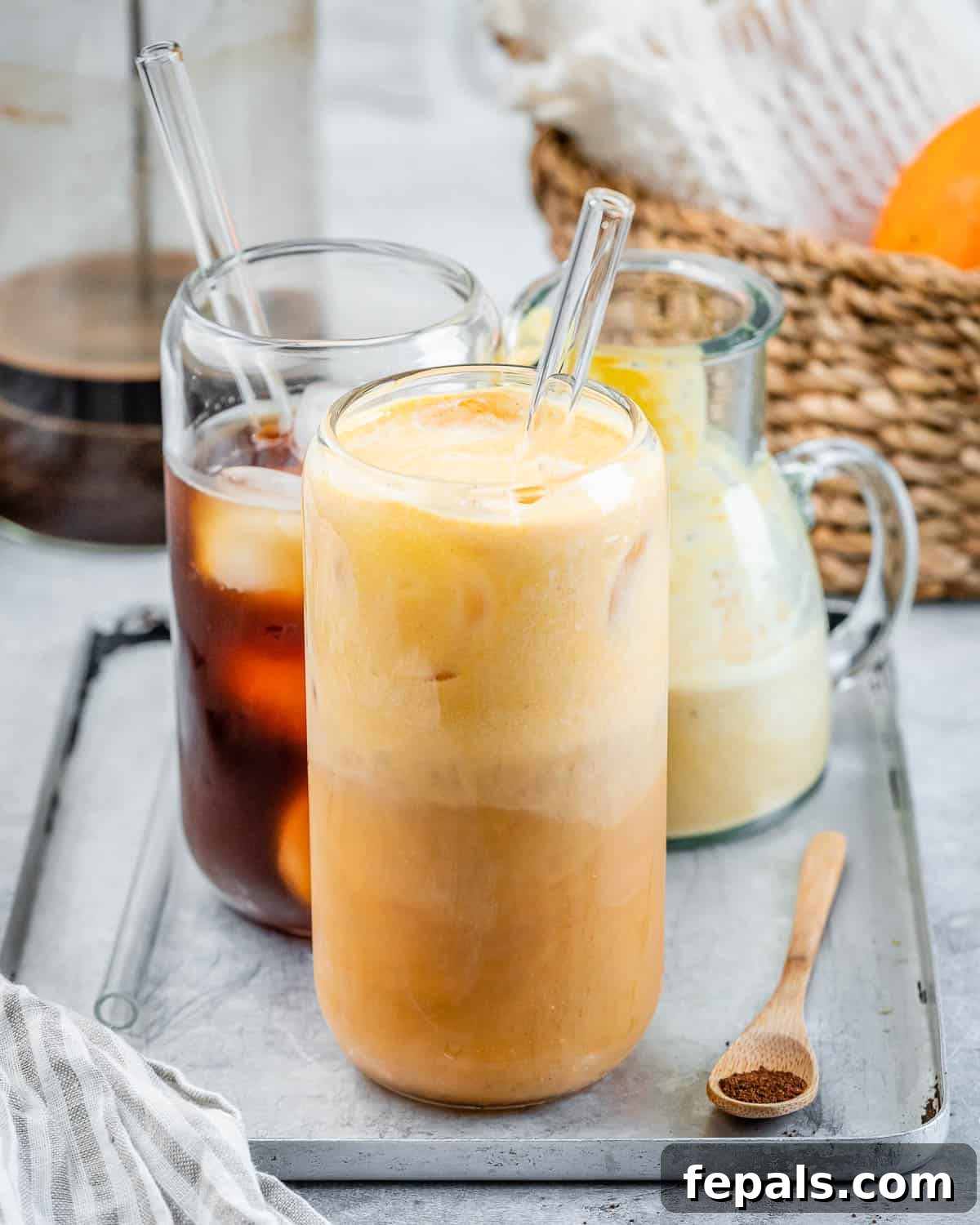 Two aesthetically arranged cups of homemade pumpkin cold brew coffee, one with a glass straw and the other without, garnished with a sprinkle of pumpkin pie spice, symbolizing a perfect fall morning beverage.