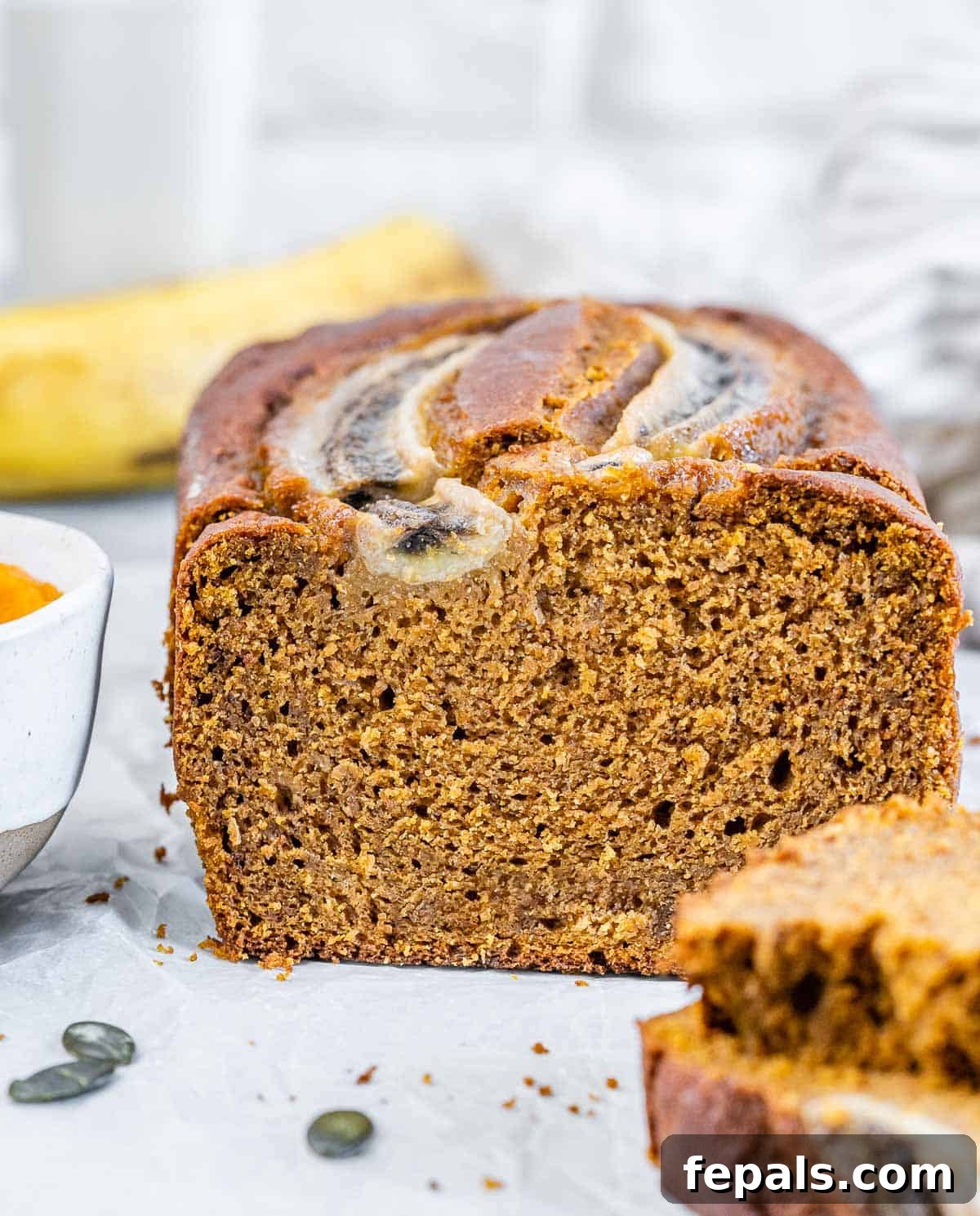 A beautifully baked loaf of pumpkin banana bread on a flat surface, with two slices already cut and ready to enjoy. The golden-brown crust and moist interior are visible.