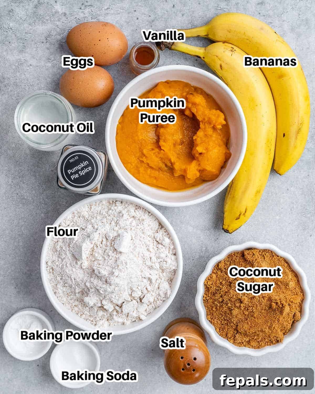 A collection of fresh ingredients laid out on a surface, including ripe bananas, a can of pumpkin puree, eggs, flour, coconut oil, and various spices, all ready to be used for making banana pumpkin bread.