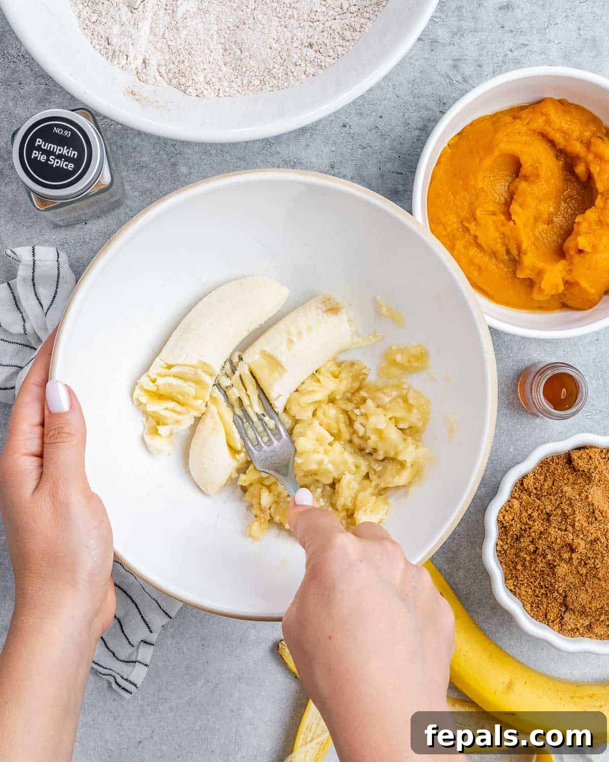 Mashing ripe bananas with a fork in a white mixing bowl, ready for the next steps in making the bread batter.