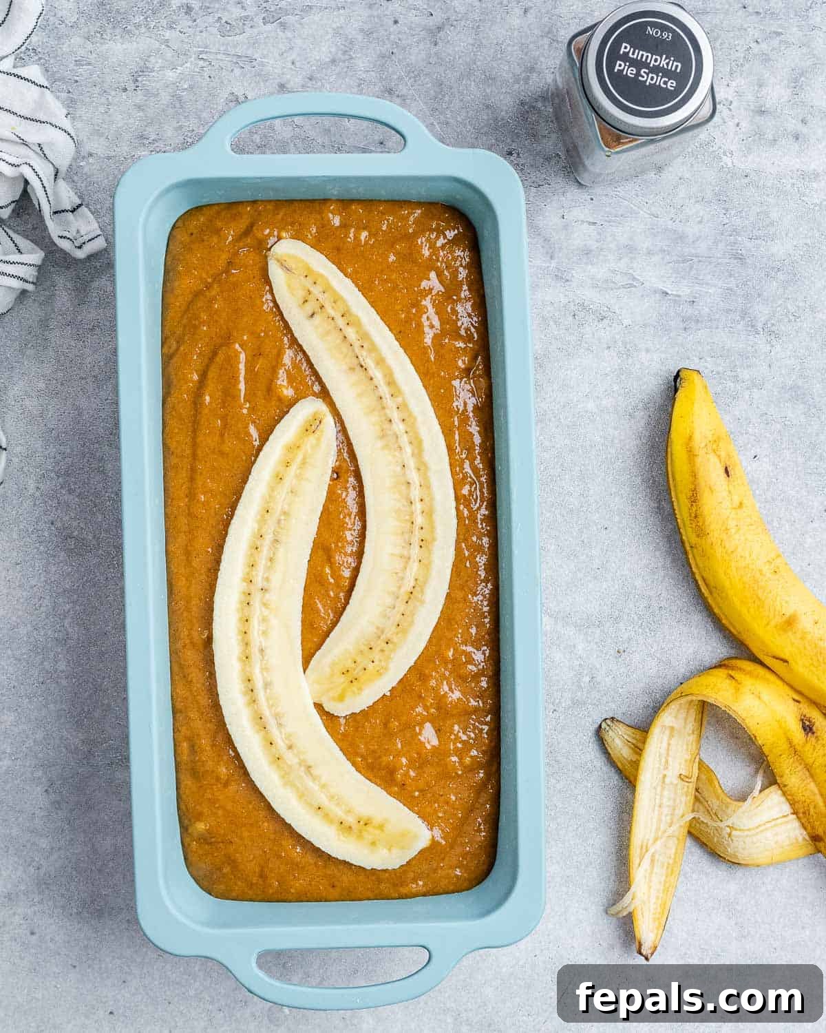 Pumpkin banana bread batter neatly poured into a parchment-lined loaf pan, adorned with decorative banana slices and pumpkin seeds on top before baking.