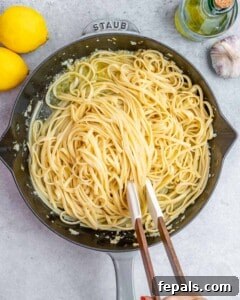 Pasta being tossed in the lemon sauce inside a black skillet.