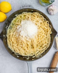 Pasta tossed in a skillet with cheese beginning to melt over the top.