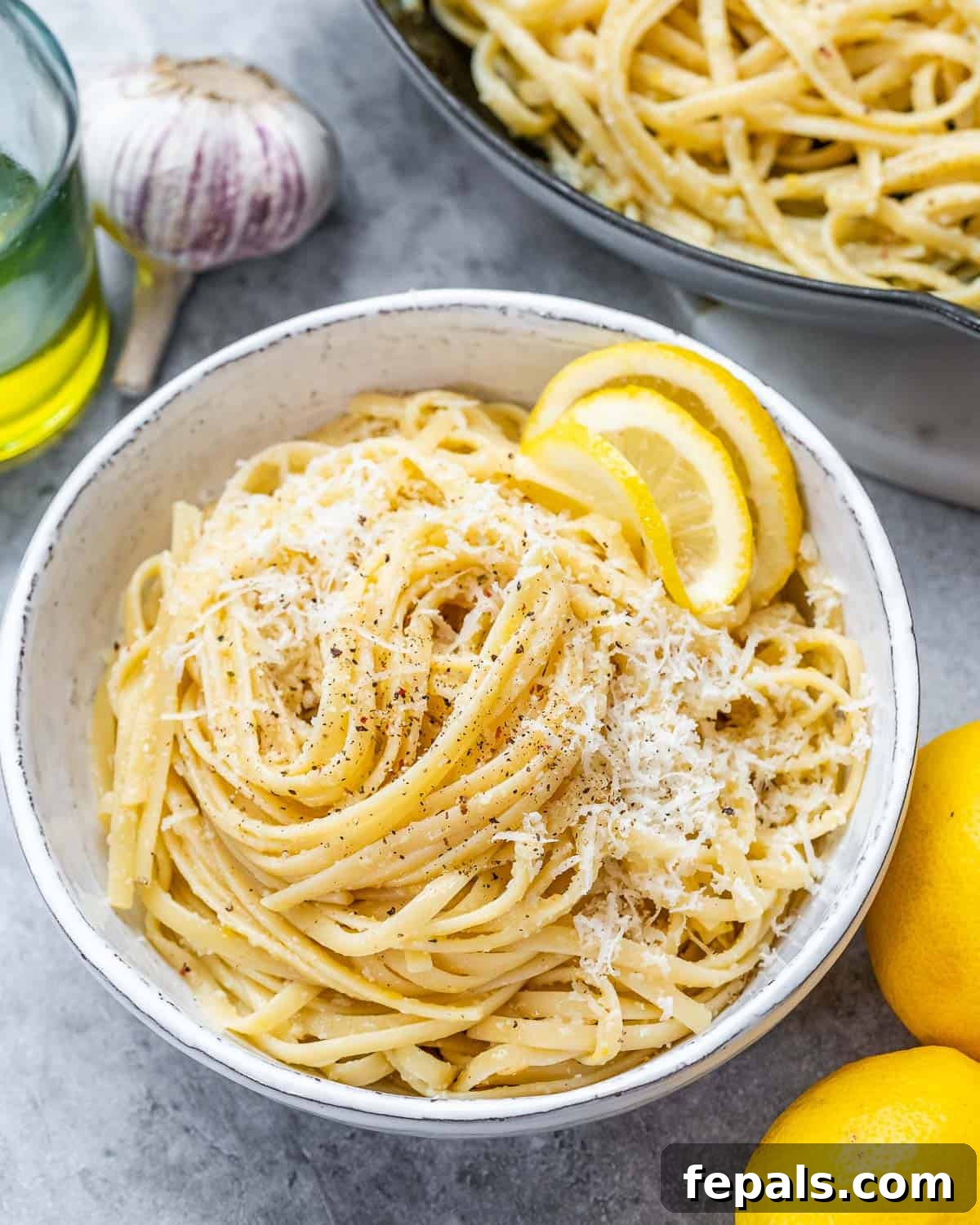 Cooked Pasta al Limone in a white bowl topped with grated parmesan, fresh lemon slices, and parsley.