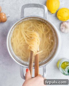 Cooked linguine being lifted from boiling salted water with kitchen tongs.