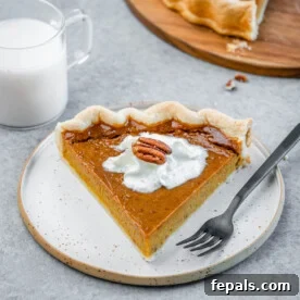 A slice of pumpkin pie on a white plate with a fork by it.