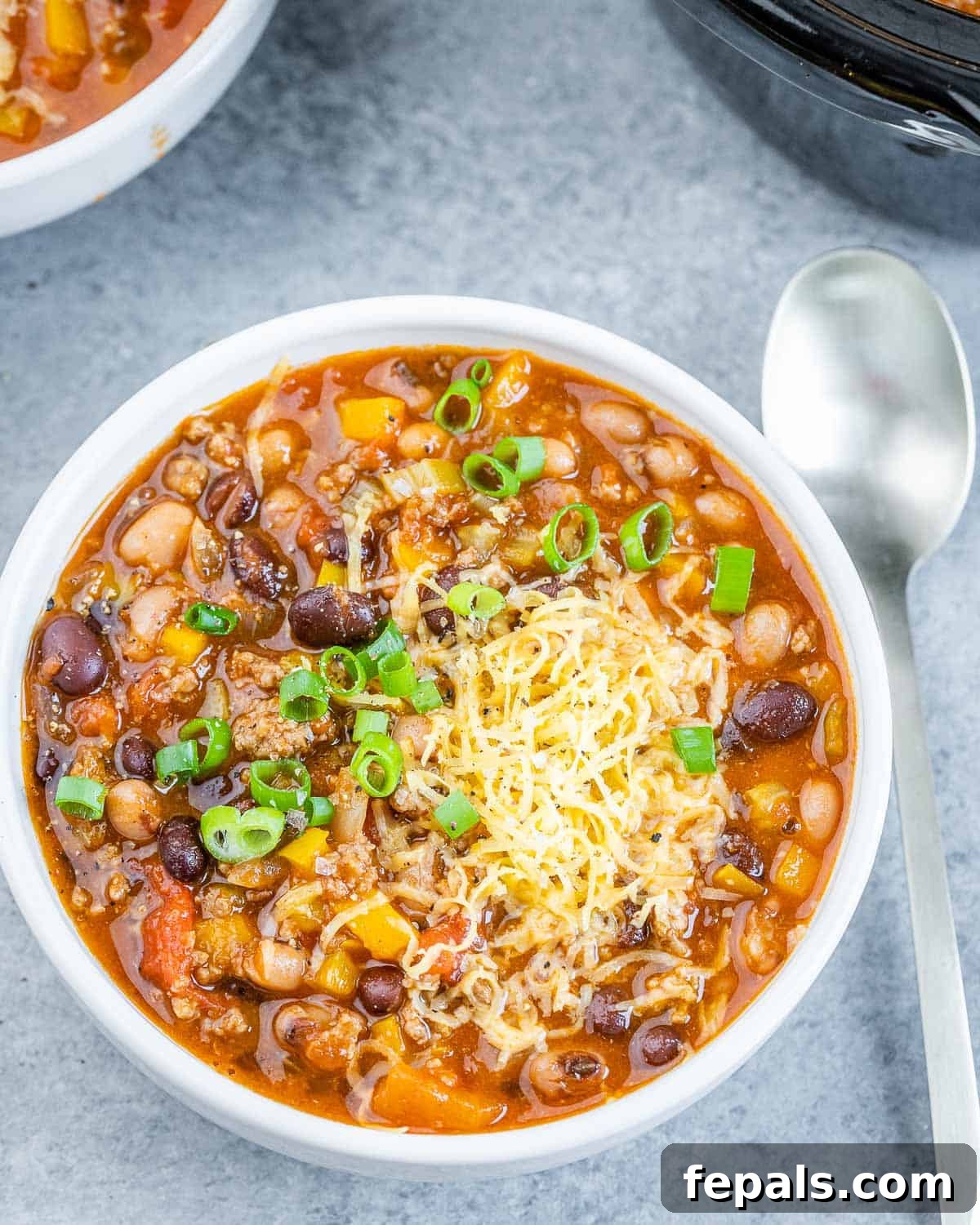 Easy Crockpot Chili 9 A bowl of flavorful chili with beans, garnished with fresh herbs, and a spoon dipped in it.
