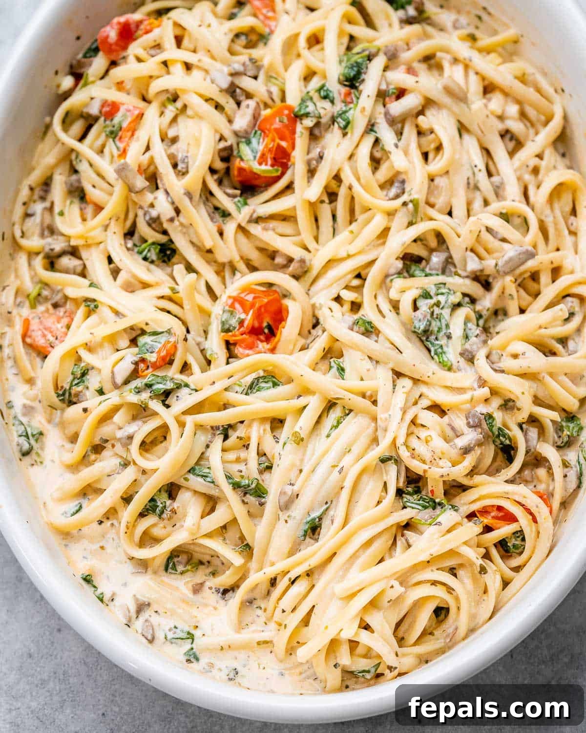 Blush Tomato Cream Pasta 11 Creamy spaghetti with roasted tomatoes and spinach in a white oval baking dish, garnished with fresh herbs.