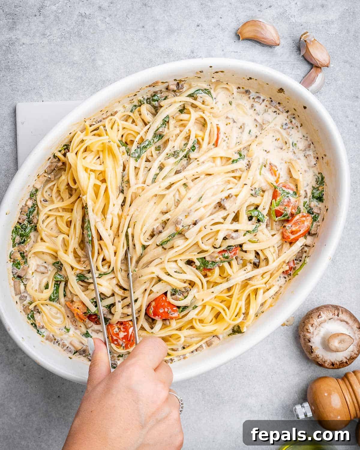 Blush Tomato Cream Pasta 9 A hand mixing the cooked pasta with the creamy tomato and vegetable sauce in a large baking dish.