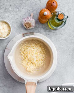 Velvety Butternut Mac and Cheese 6 Shredded cheese is added to a pot with white sauce for mac and cheese.