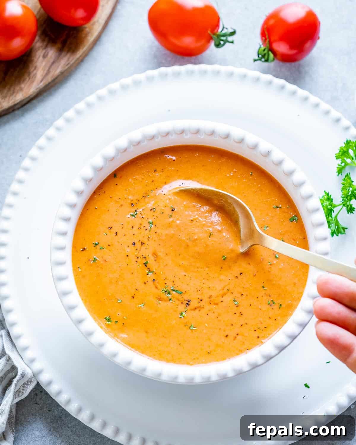 Smoked Tomato Bisque 2 A white bowl of rich, creamy roasted tomato soup with a spoon resting in it, garnished with fresh herbs.