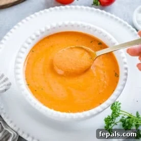 Smoked Tomato Bisque 13 creamy orange looking tomato soup in a white round bowl with spoonful of soup.