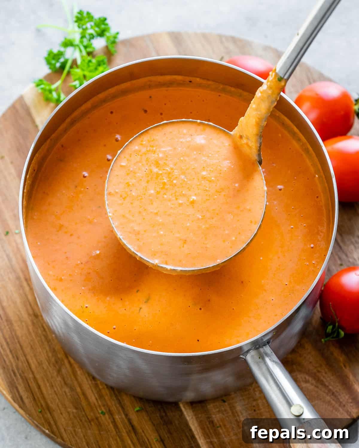 Smoked Tomato Bisque 3 A large pot brimming with vibrant orange roasted tomato soup, a ladle dipping into its creamy texture, ready to serve.