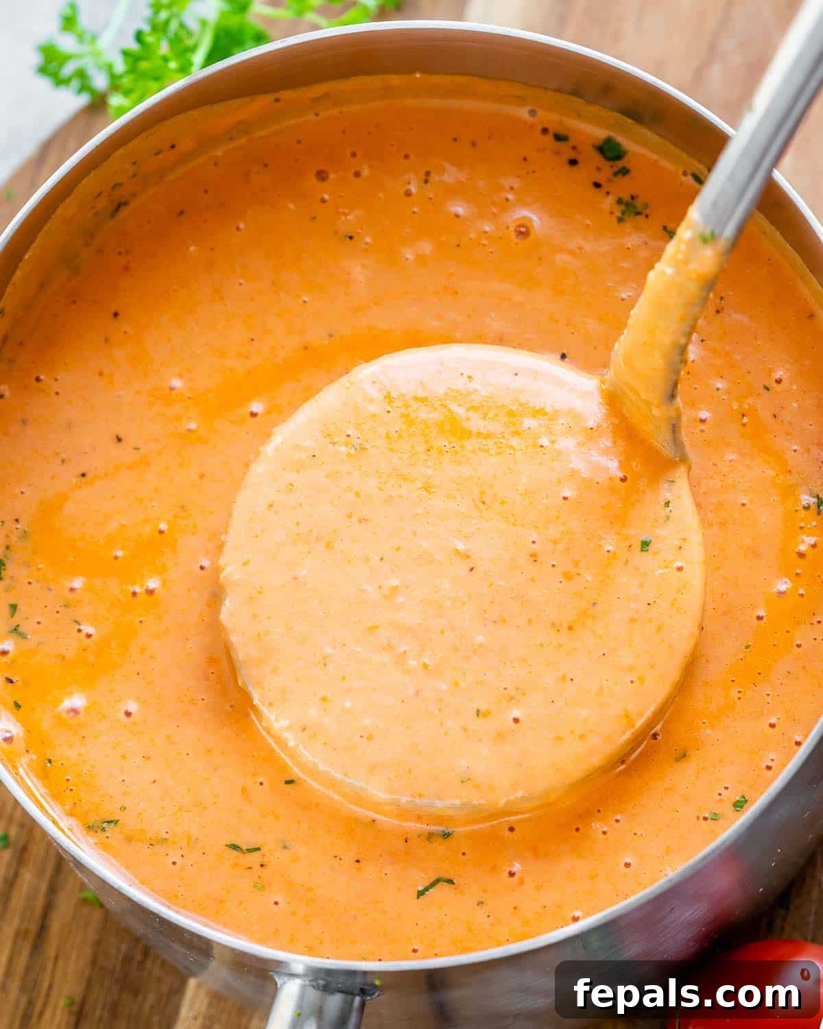 Smoked Tomato Bisque 9 A pot of finished creamy roasted tomato soup, with a spoonful being lifted, showing its smooth, inviting texture.
