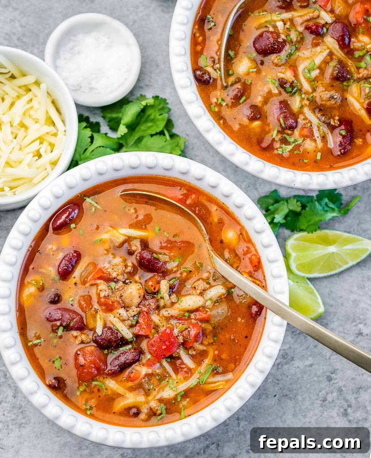 Two white bowls of chili with spoon in the bowl.