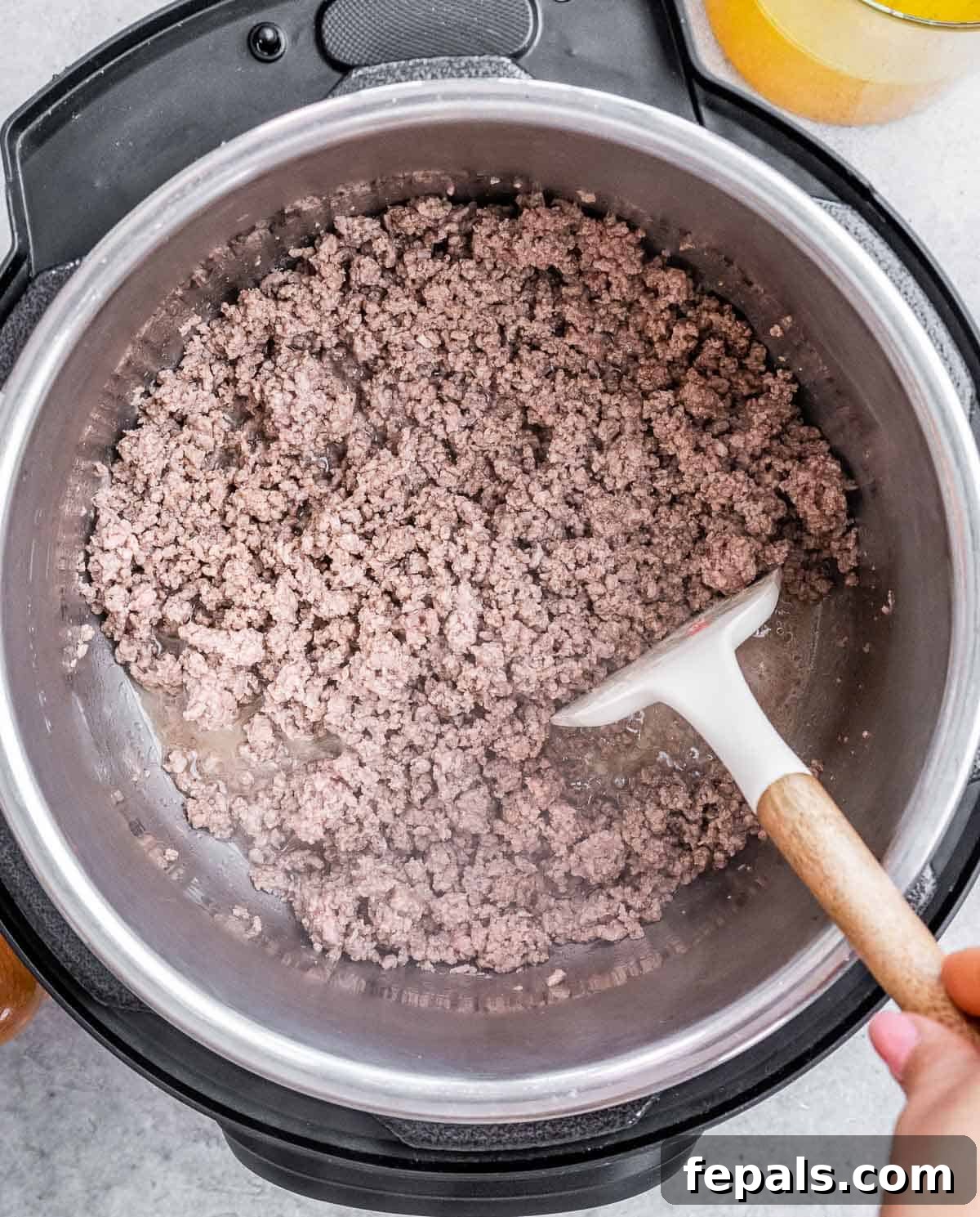 A white spatula stirring a pot with cooked ground beef.