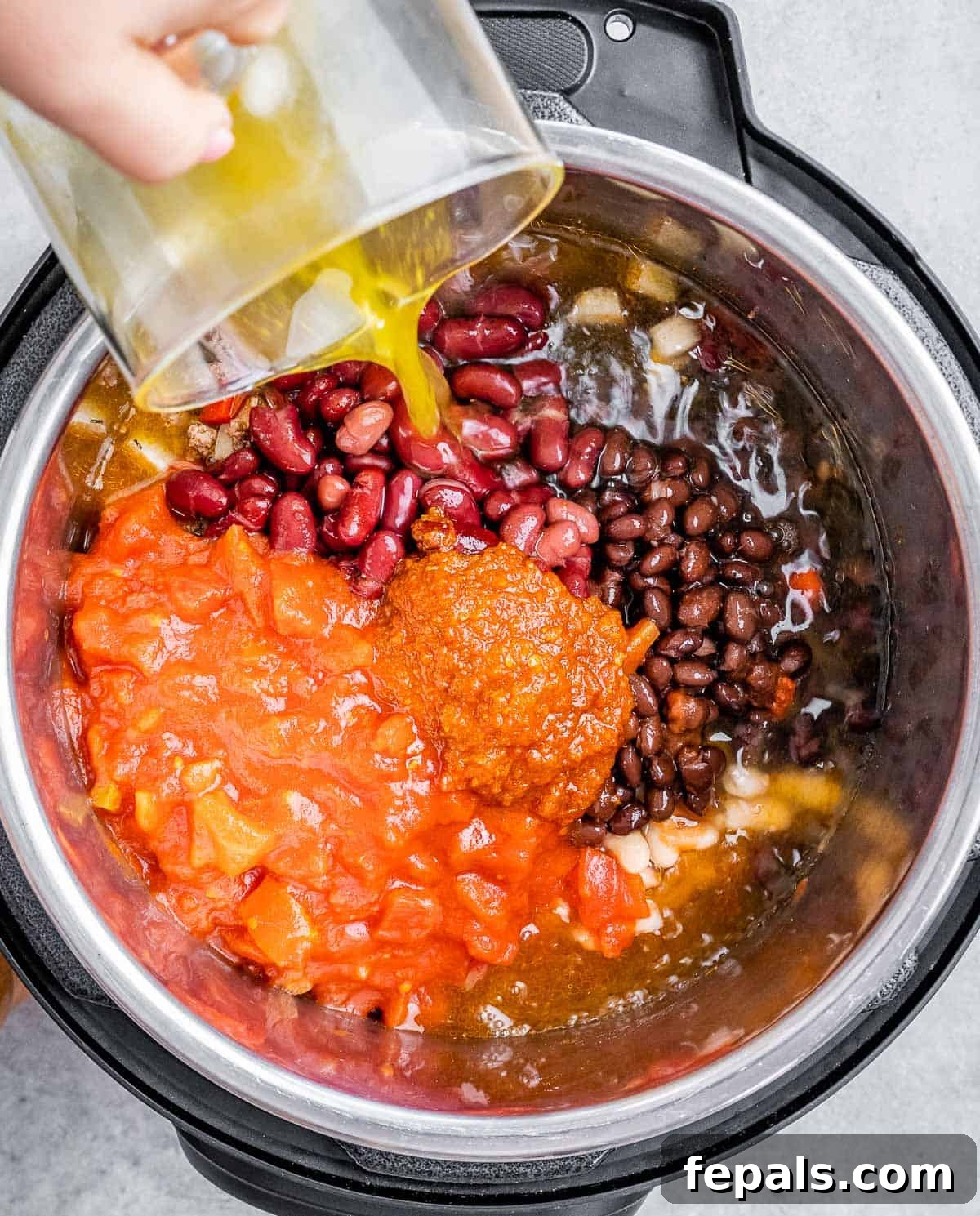 Pouring liquid into a pot filled with beans and tomatoes.