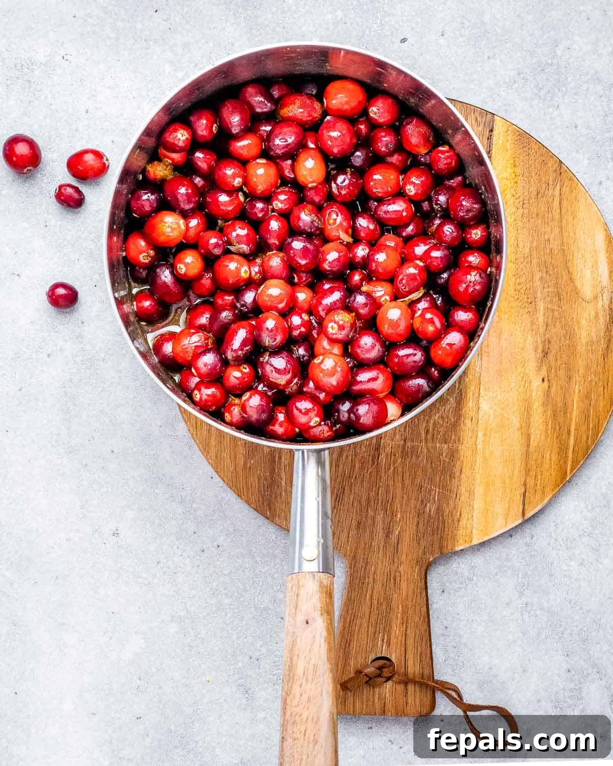 Vibrant Cranberry Orange Relish 4 Adding cranberries: Fresh or frozen cranberries are stirred into the bubbling orange juice and maple syrup mixture in a saucepan.