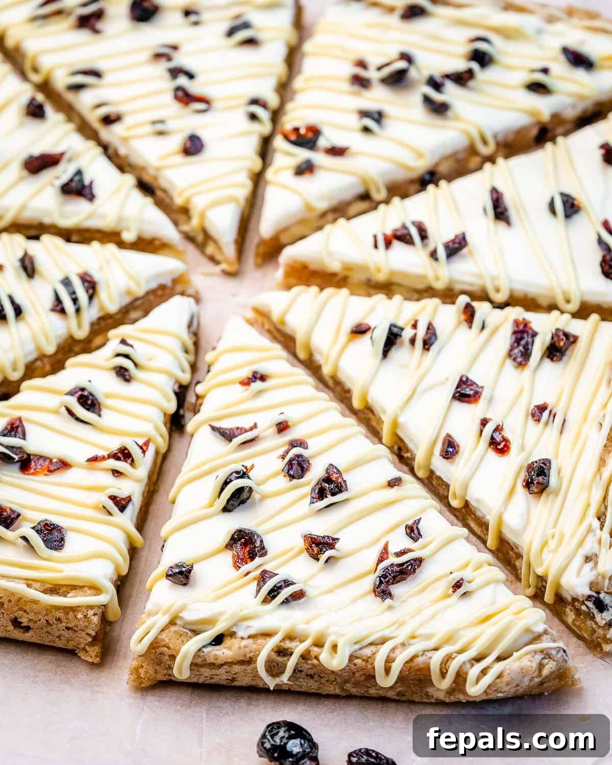 Close-up shot of freshly cut bliss bars on parchment paper, showing the frosting and cranberry toppings.