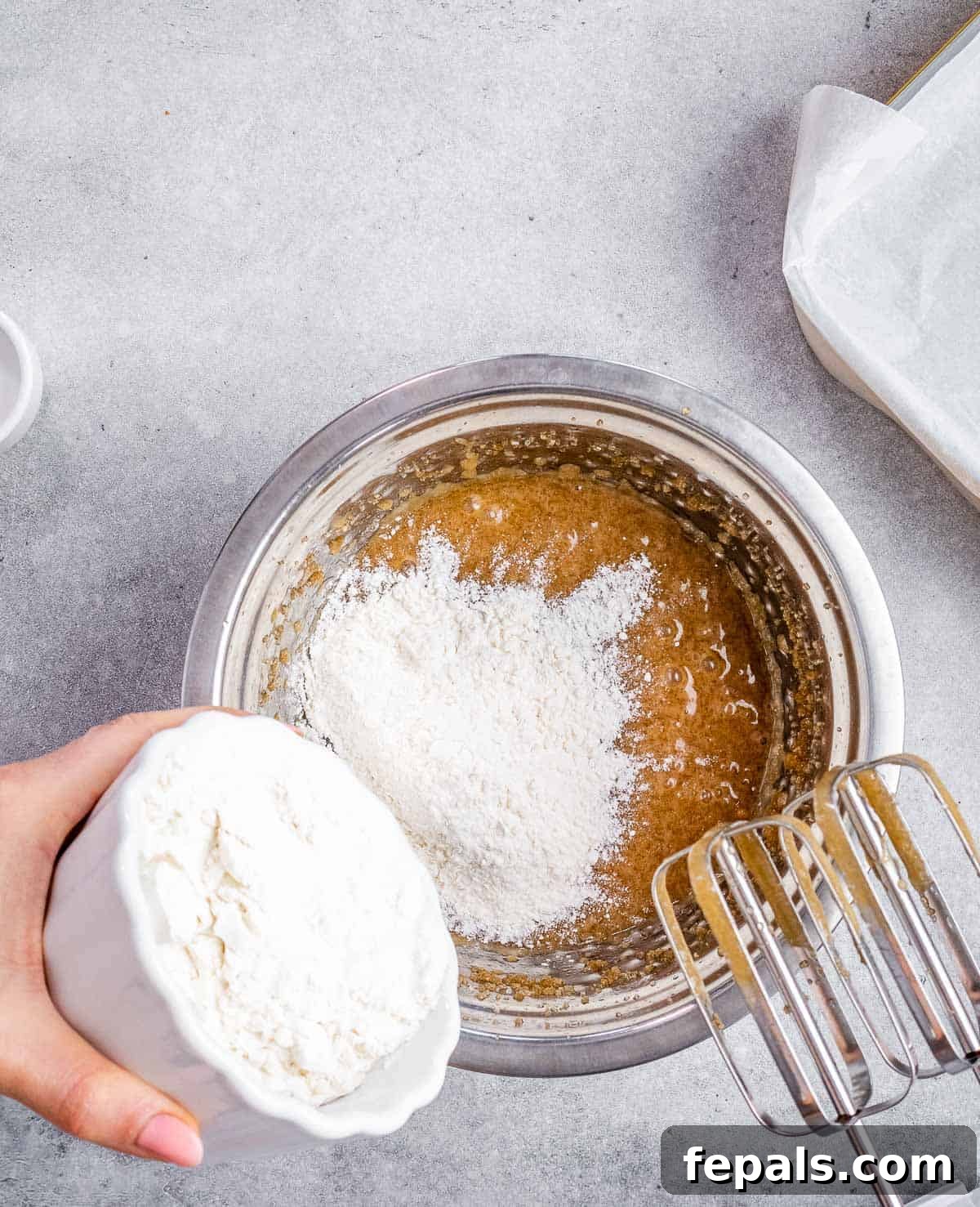 Flour being gently poured into a bowl containing the wet batter mixture.