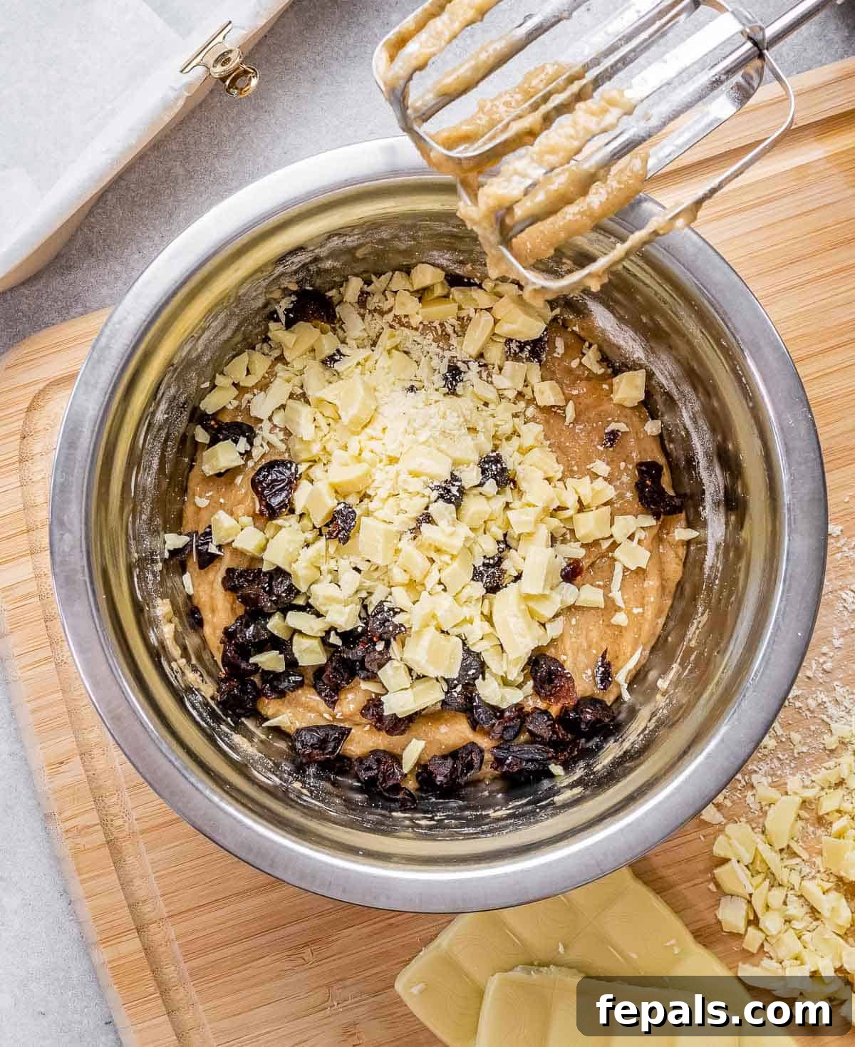 A bowl of batter with dried cranberries and chopped white chocolate being folded in.