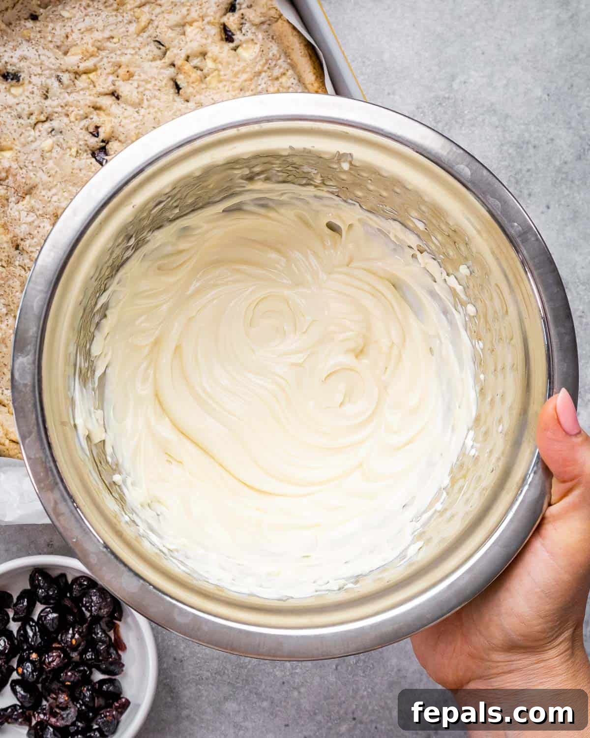 A hand holding a bowl of smooth, creamy cream cheese frosting mixture.