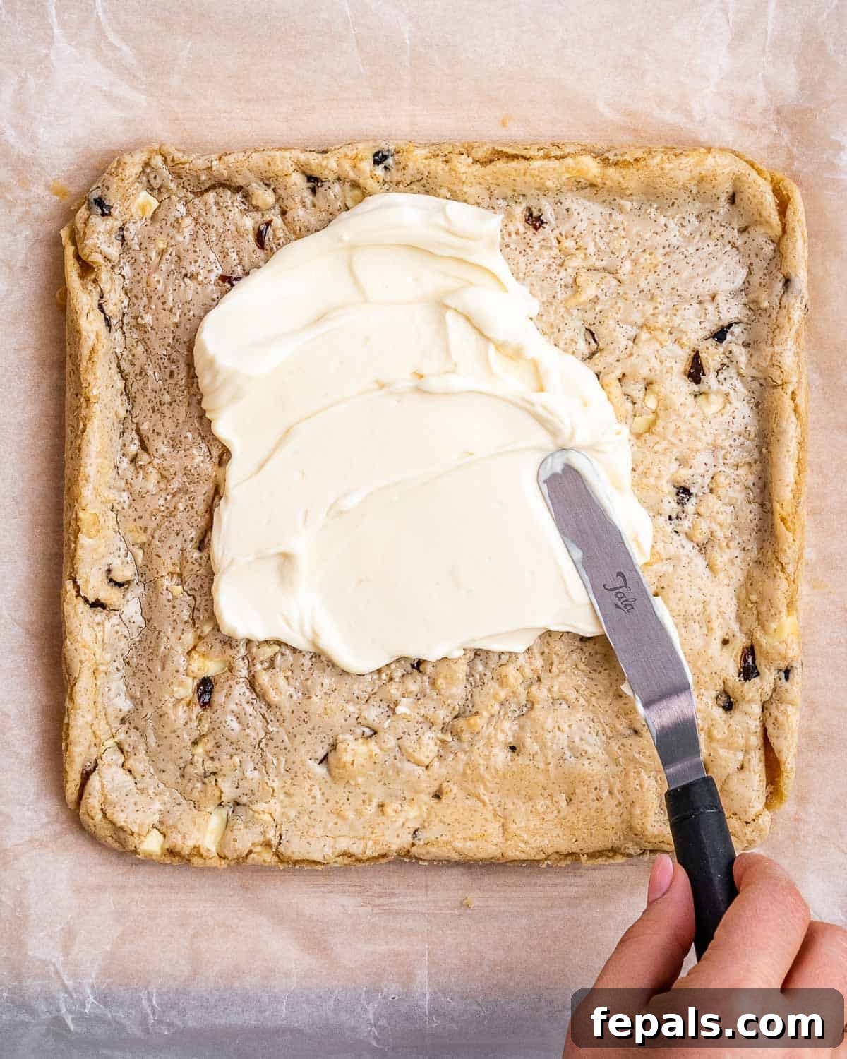 Cream cheese frosting being spread evenly over the cooled cranberry bliss bar base.