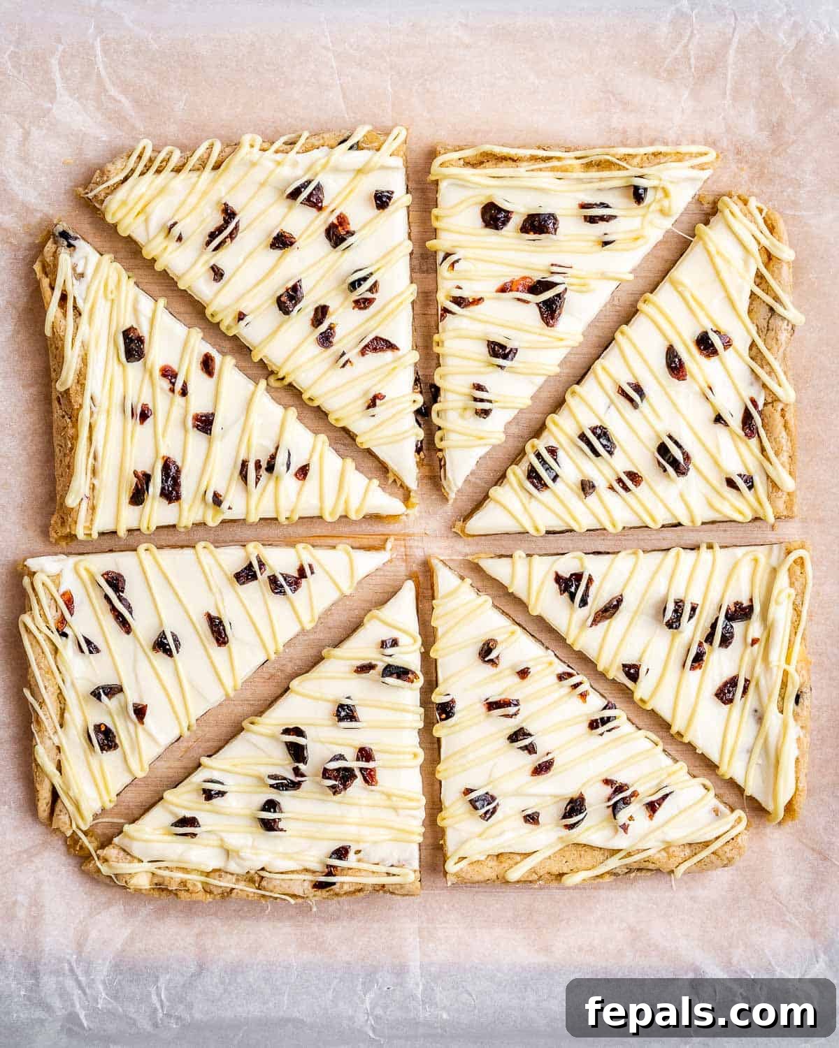 Cranberry bliss bars cut into eight triangular pieces on parchment paper, ready for serving.