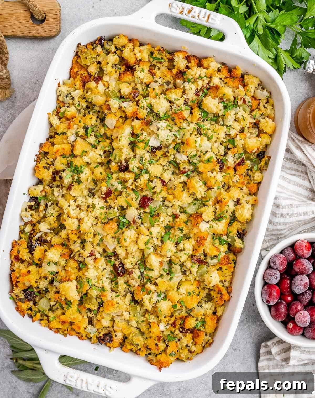A white casserole dish with cornbread stuffing in it, garnished with fresh herbs.