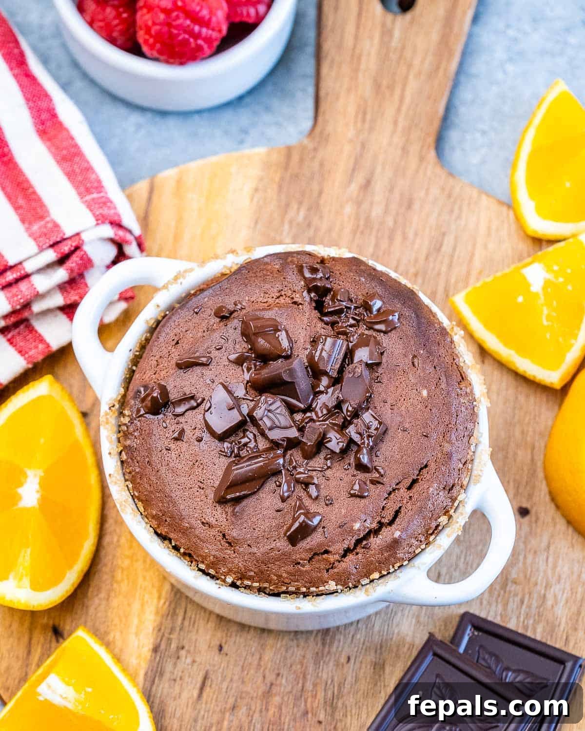 Freshly baked Chocolate Soufflé in a white ramekin, topped with delicate chocolate shavings and garnished with vibrant orange slices, ready to be served.