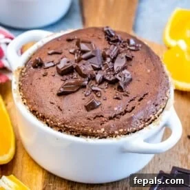 Baked Chocolate Soufflé in a white ramekin, sprinkled with chocolate pieces and presented with fresh orange slices.