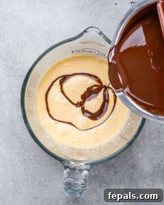Melted chocolate being poured into the whipped egg yolk and sugar mixture in a glass bowl.